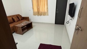 A room with a brown sofa, a wooden coffee table, a television mounted on the wall, and a door with a handle. - 1 bhk comfy stay 1 (Pune)