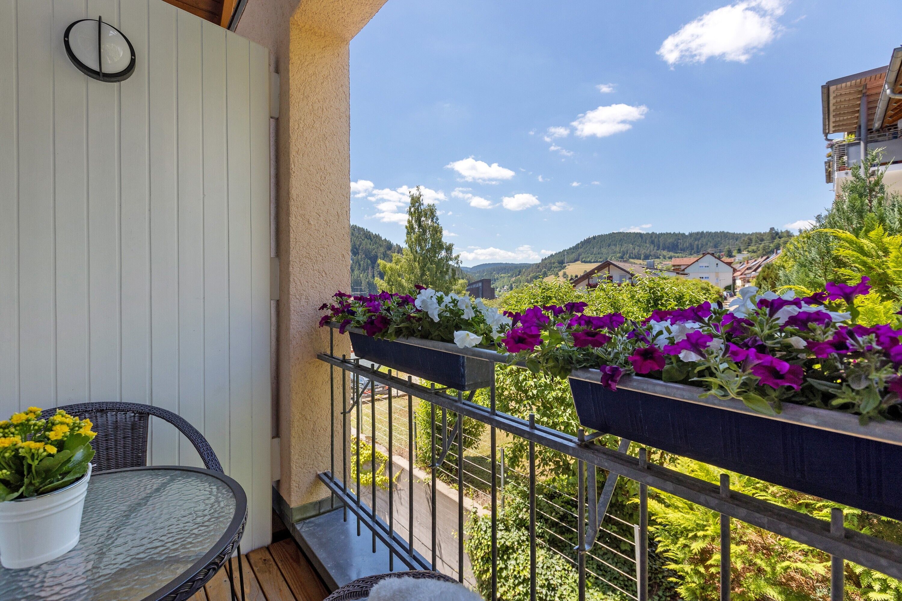 A balcony with a table and chairs, potted plants, and a view of a mountainous landscape.