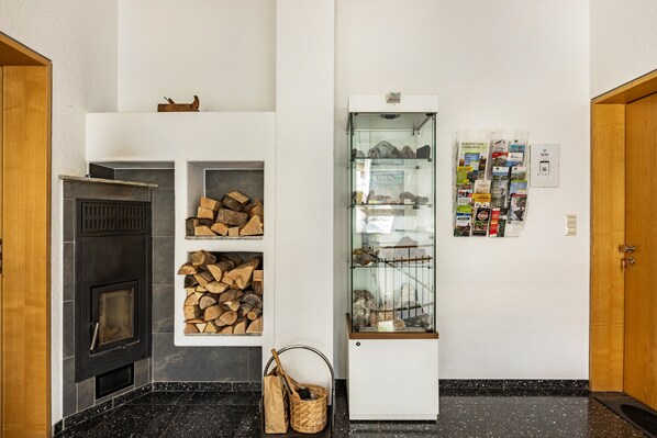 Une pièce avec une cheminée, des étagères remplies de bois de chauffage, une vitrine contenant des brochures et une porte en bois.