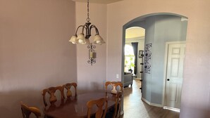 Un comedor con una mesa y sillas de madera, una araña y un pasillo que conduce a otra habitación.