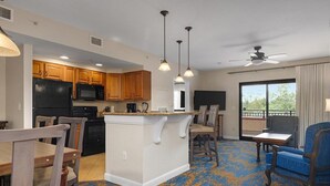 Amplia sala de estar con una isla central, muebles de madera, un refrigerador negro, un microondas y un ventilador de techo.