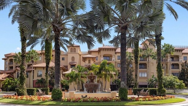 Un hotel con una fuente, palmeras y un césped bien cuidado.