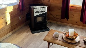 Ein gemütliches Ferienhäuschen im Inneren mit Holzvertäfelung, einem an der Wand montierten Fernseher, einem Kaminofen, einer Couch und einem Tisch mit Kerze und Dekorationsobjekten.