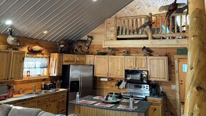 Ein rustikales Blockhaus im Inneren mit einer Küche, Holzbalkendecke und einem Essbereich mit Hockern.