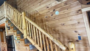 Eine Holztreppe mit Handlauf, einer Deckenleuchte und einem an der Wand befestigten Thermostat.
