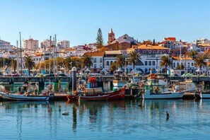 A marina with boats docked, a prominent church with a bell tower, and residential buildings in the background.