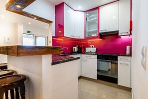 A modern kitchen with white cabinets, a pink accent wall, and a wooden bar counter.