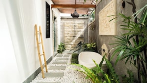 A narrow, stone-walled corridor with a wooden ladder, a stone wall with a carved design, and a bathtub in a corner.