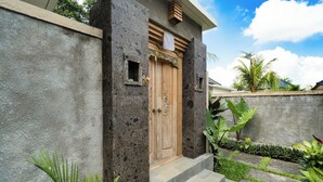 A stone facade with a wooden door, steps leading to a porch, and tropical plants.