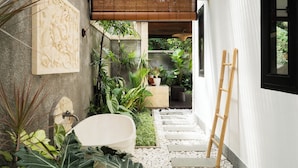 A narrow garden pathway with stepping stones, surrounded by lush greenery and a white wall.