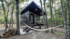 Une cabane moderne dotée d’une façade en verre, d’une terrasse en bois et d’un hamac.