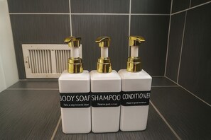 Drie flessen douchezeep, shampoo en conditioner op een betegelde vloer.