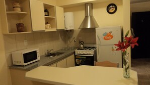 A compact kitchen with white cabinets, a microwave, a gas stove, and a refrigerator. - Apart Avenida (Concordia)