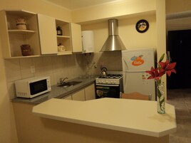 Una cocina compacta con armarios blancos, un microondas, una estufa a gas y un refrigerador.