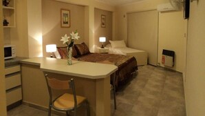 A compact hotel room with a bed, bedside tables, a desk with a chair, and a small kitchenette. - Apart Avenida (Concordia)