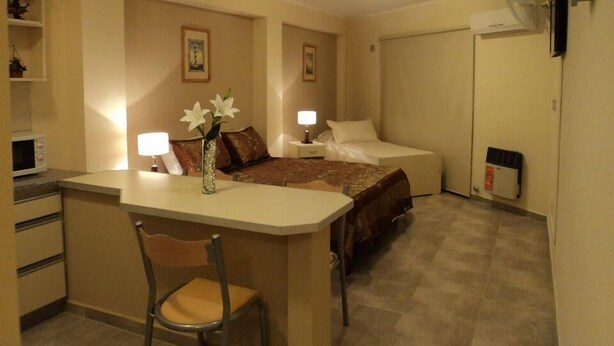 A compact hotel room with a bed, bedside tables, a desk with a chair, and a small kitchenette. - Apart Avenida (Concordia)