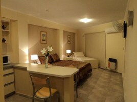 Habitación de hotel pequeña con cama, mesitas de noche, escritorio con silla y una kitchenette.