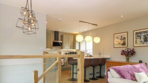 A modern kitchen with wooden flooring, a dining area with bar stools, and a staircase leading to an upper level. - Ashlea (Lauder)