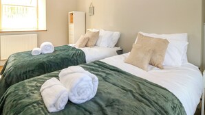 A hotel room with two beds, each with a green bedspread and white pillows. There are rolled towels on the beds. - Ashlea (Lauder)