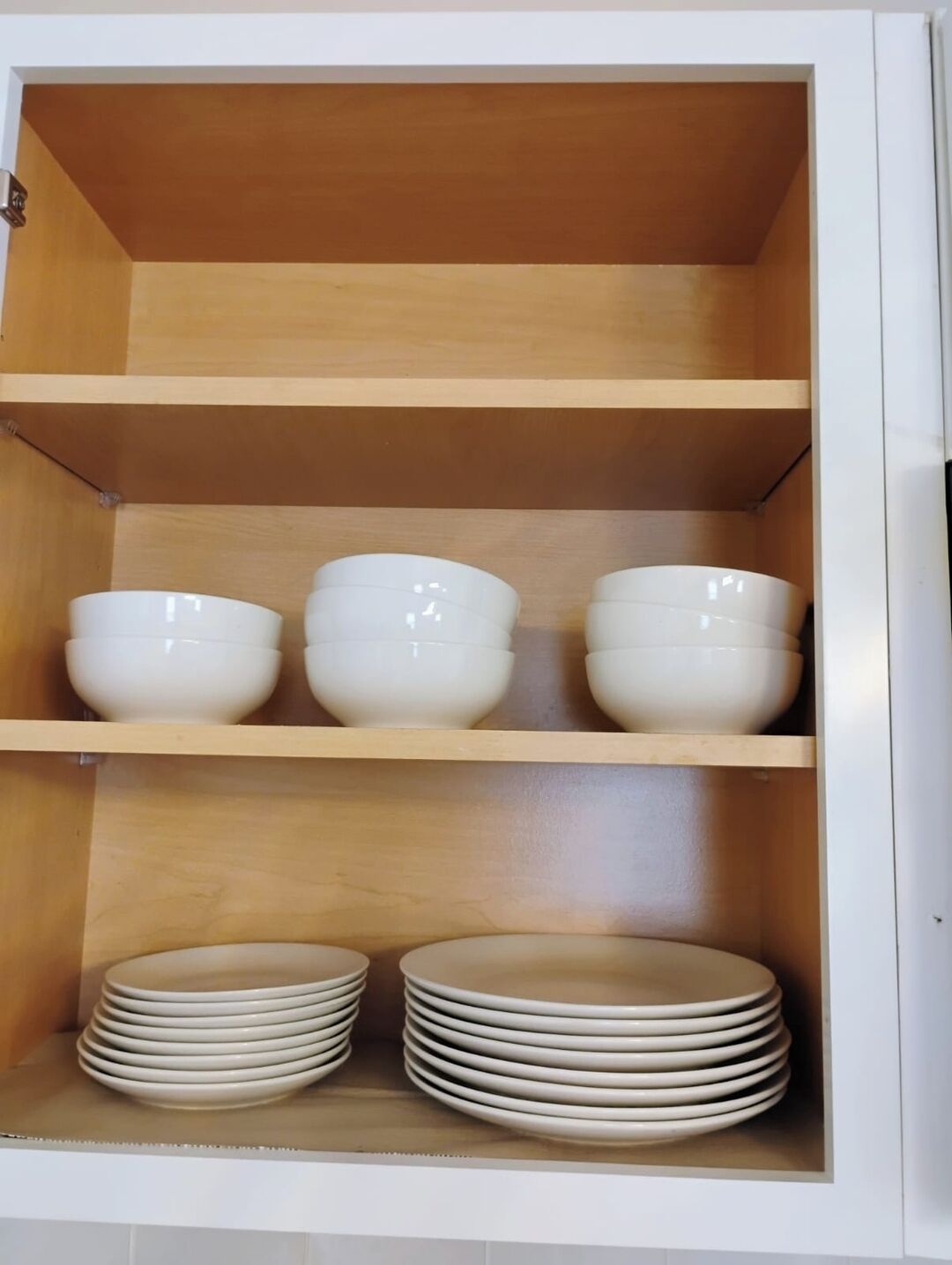 Een kast met drie planken, elk gevuld met witte kommen en borden.