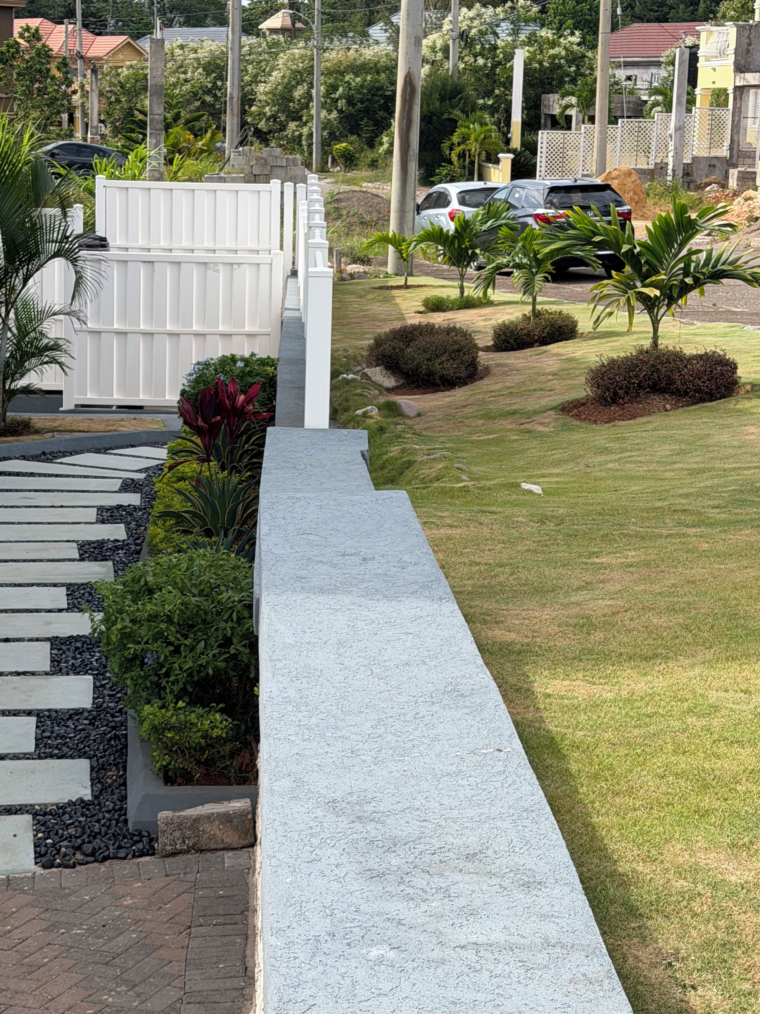 A residential area with a paved walkway, a white fence, and a grassy lawn.