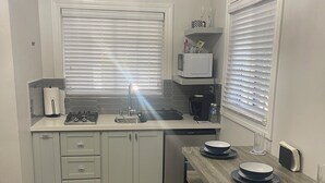 Une cuisine compacte avec des meubles blancs, un four à micro-ondes, un évier et un coin repas comprenant une table et des bancs en bois.