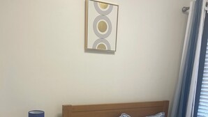 Une chambre à coucher bien rangée, avec un lit, une table de chevet dotée d’une lampe et un tableau accroché au mur.