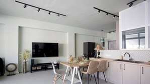 A modern kitchen with a dining area, featuring a large flat-screen TV, a dining table set for four, and a built-in oven.