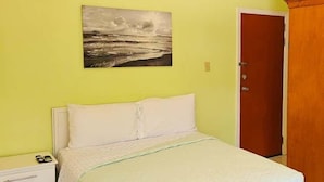 Un dormitorio con cama, mesita de noche, una puerta y un cuadro en la pared.