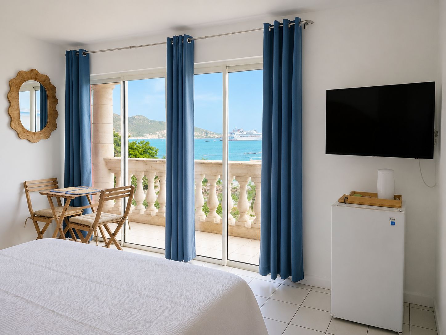 Une chambre d’hôtel comprenant un lit, un bureau avec des chaises, une télévision et un balcon avec des rideaux.