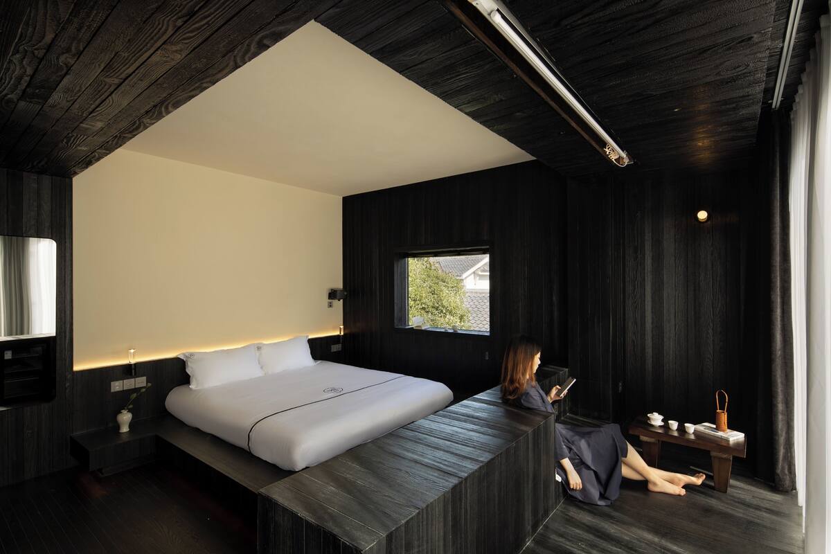 A modern bedroom with a large bed, a bedside table, a small window, and a nightstand.