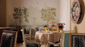 Un comedor con una mesa dispuesta para el desayuno, sillas y un mural de árboles y pájaros en la pared.