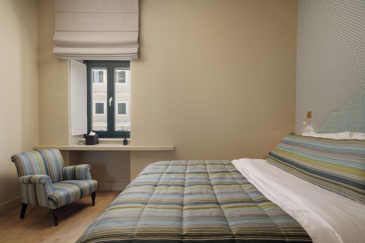 A bedroom with a large bed, a chair, a window with a view, and a wall with a geometric pattern.