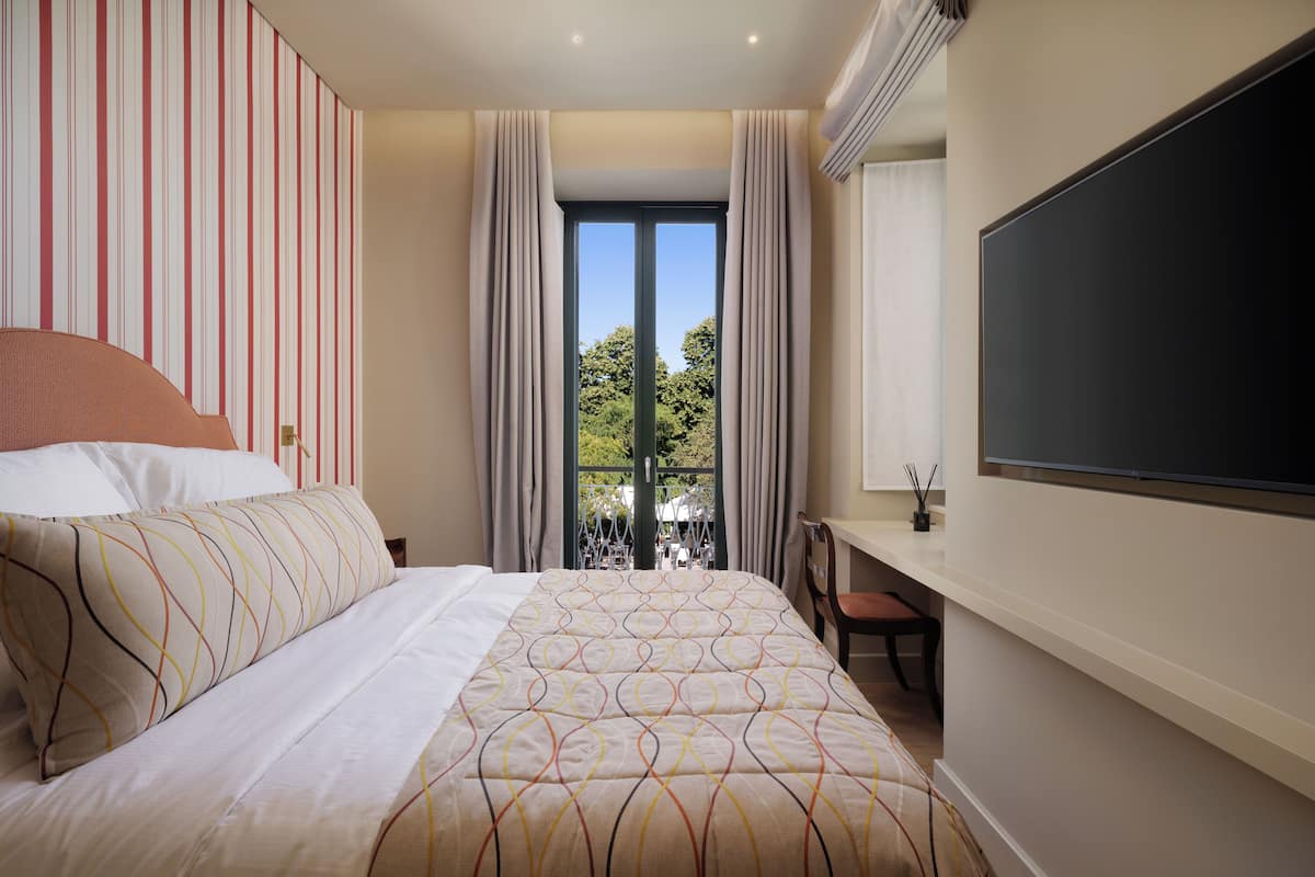 A bedroom with a bed, a desk, and a large window with curtains.