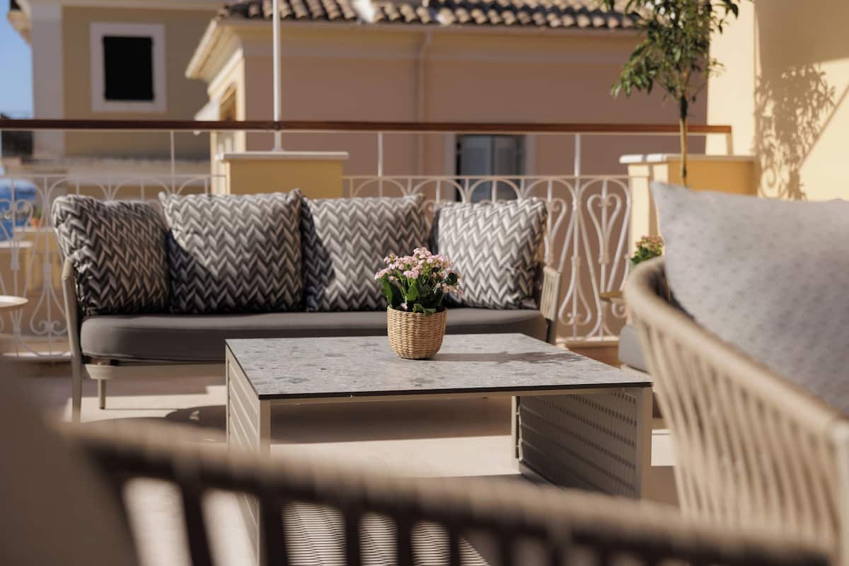 A modern outdoor seating area with a sofa and a chair, a small table with a plant, and a railing in the background.