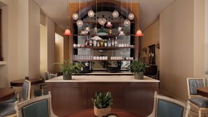 Una zona de bar con mostrador de madera, estantes con botellas y una lámpara colgante.