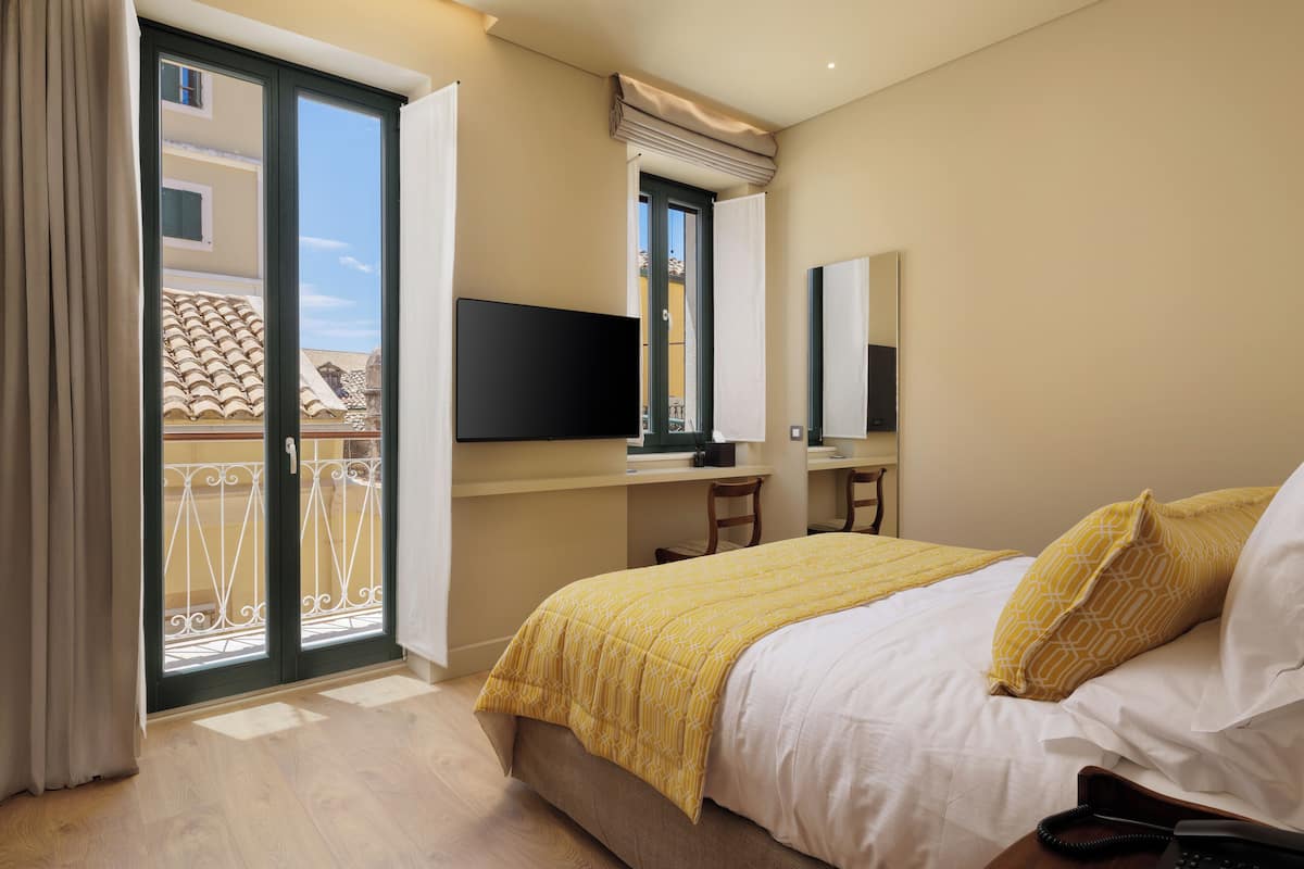A hotel room with a bed, a desk, a chair, a TV, and a balcony with a railing.
