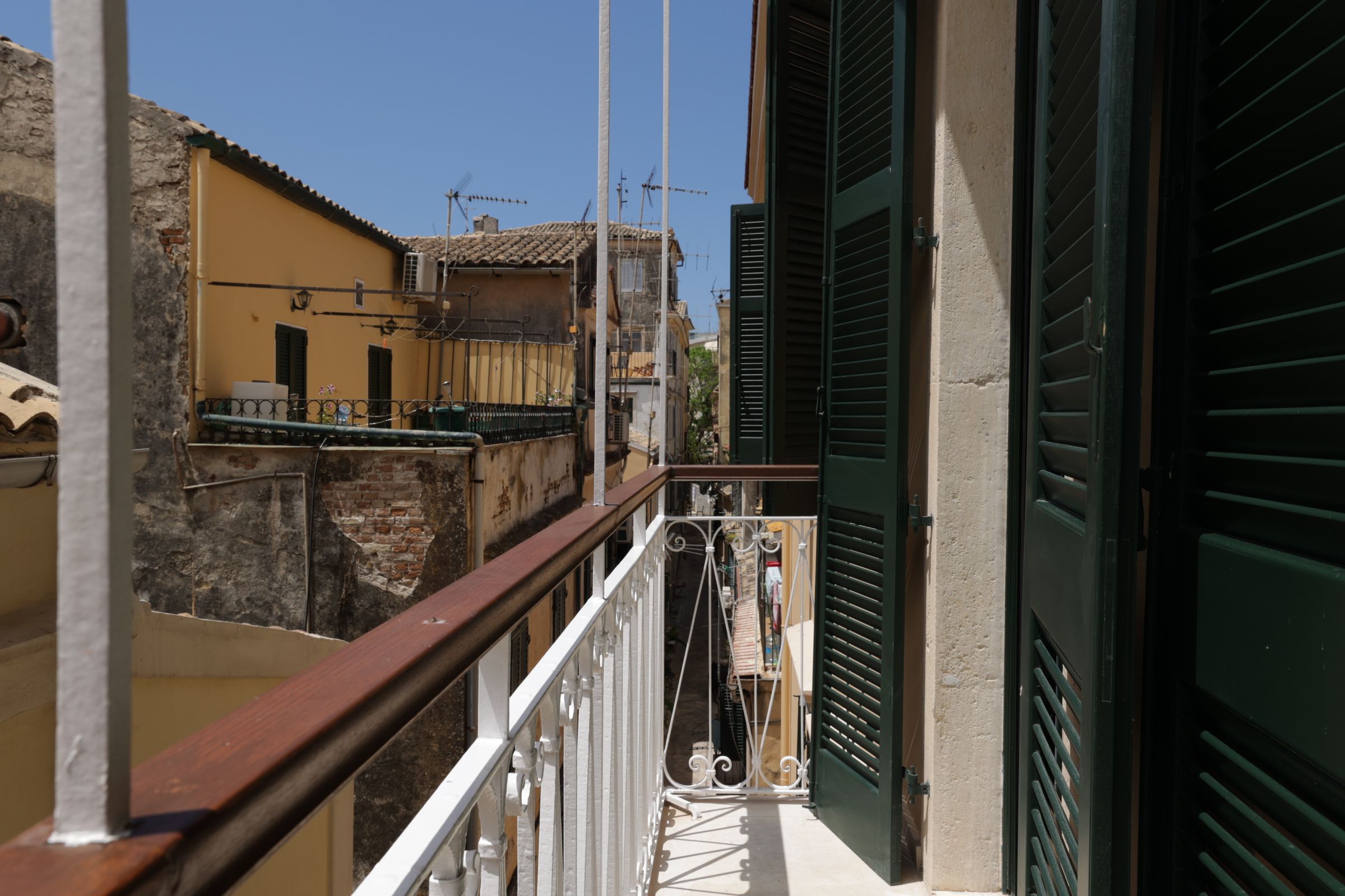 A balcony with a metal railing, a view of adjacent buildings, and a door with a green shutter.