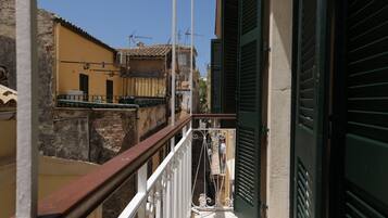 A balcony with a metal railing, a view of adjacent buildings, and a door with a green shutter.