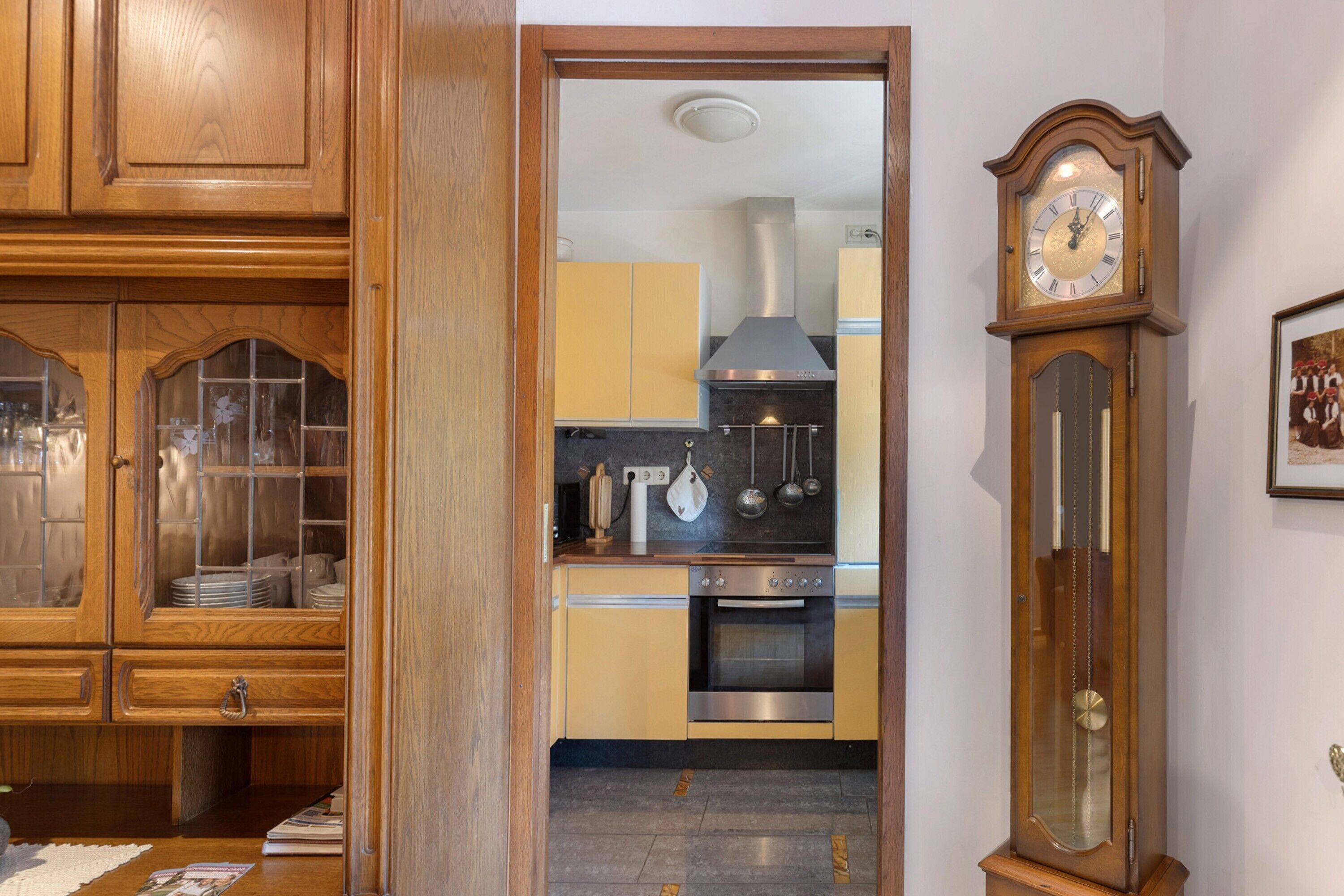 Een keuken met houten kasten, een oven van roestvrij staal en een wandklok.