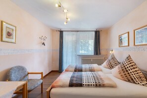 Une chambre à coucher avec un lit, deux oreillers, une chaise, une table et une fenêtre avec des rideaux.