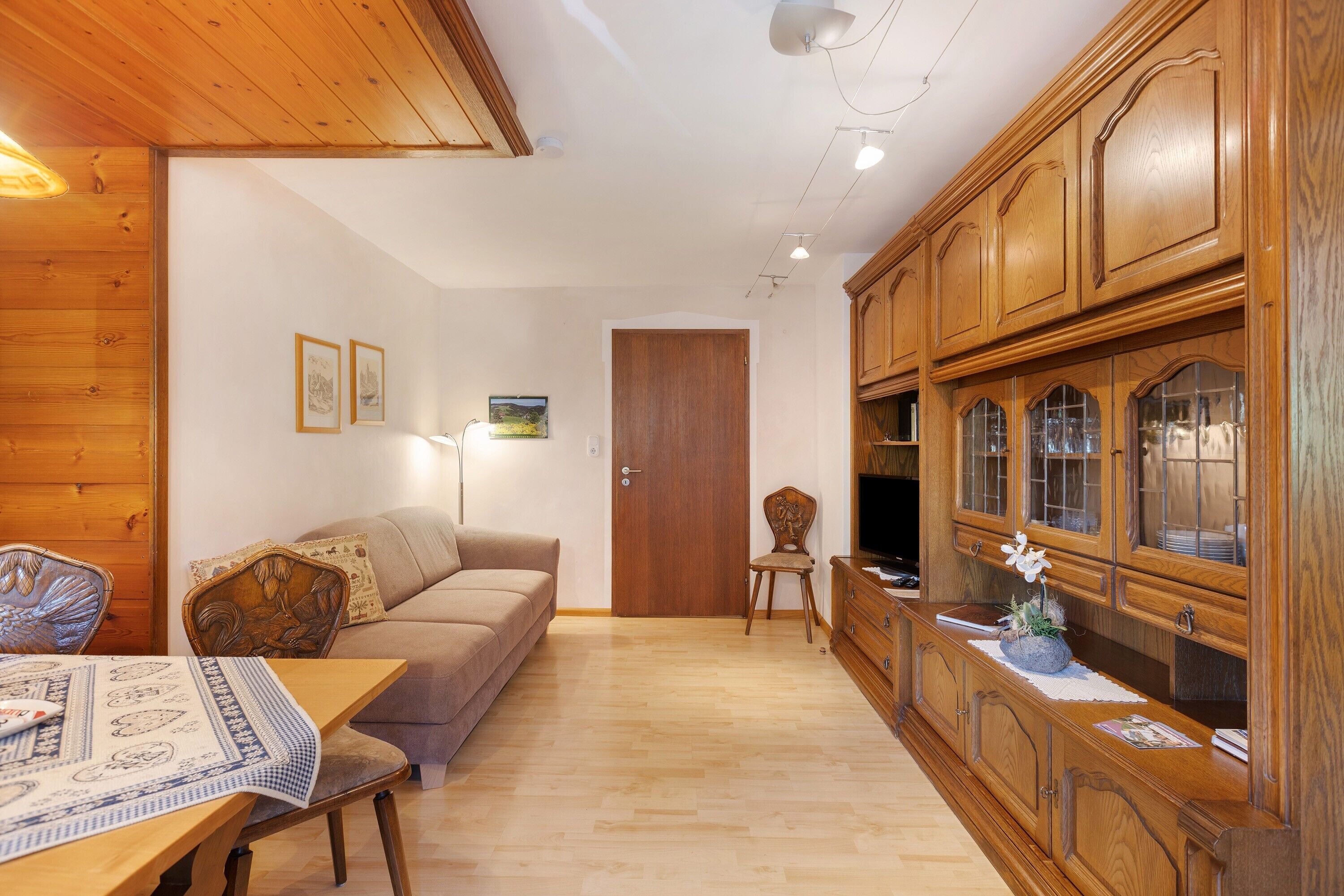 A wooden-paneled room with a sofa, a dining table with a placemat, and a wooden cabinet with glass doors.