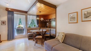 Un salon chaleureux avec un canapé, une table à manger et des chaises, un balcon décoré d’un sapin de Noël et des tableaux encadrés accrochés au mur.