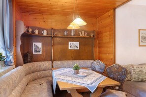Une pièce chaleureuse avec un plafond en bois, une table recouverte d’une nappe à motifs, un banc et un luminaire suspendu.