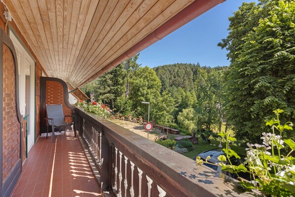 Un balcon en bois offrant une vue sur une colline boisée.