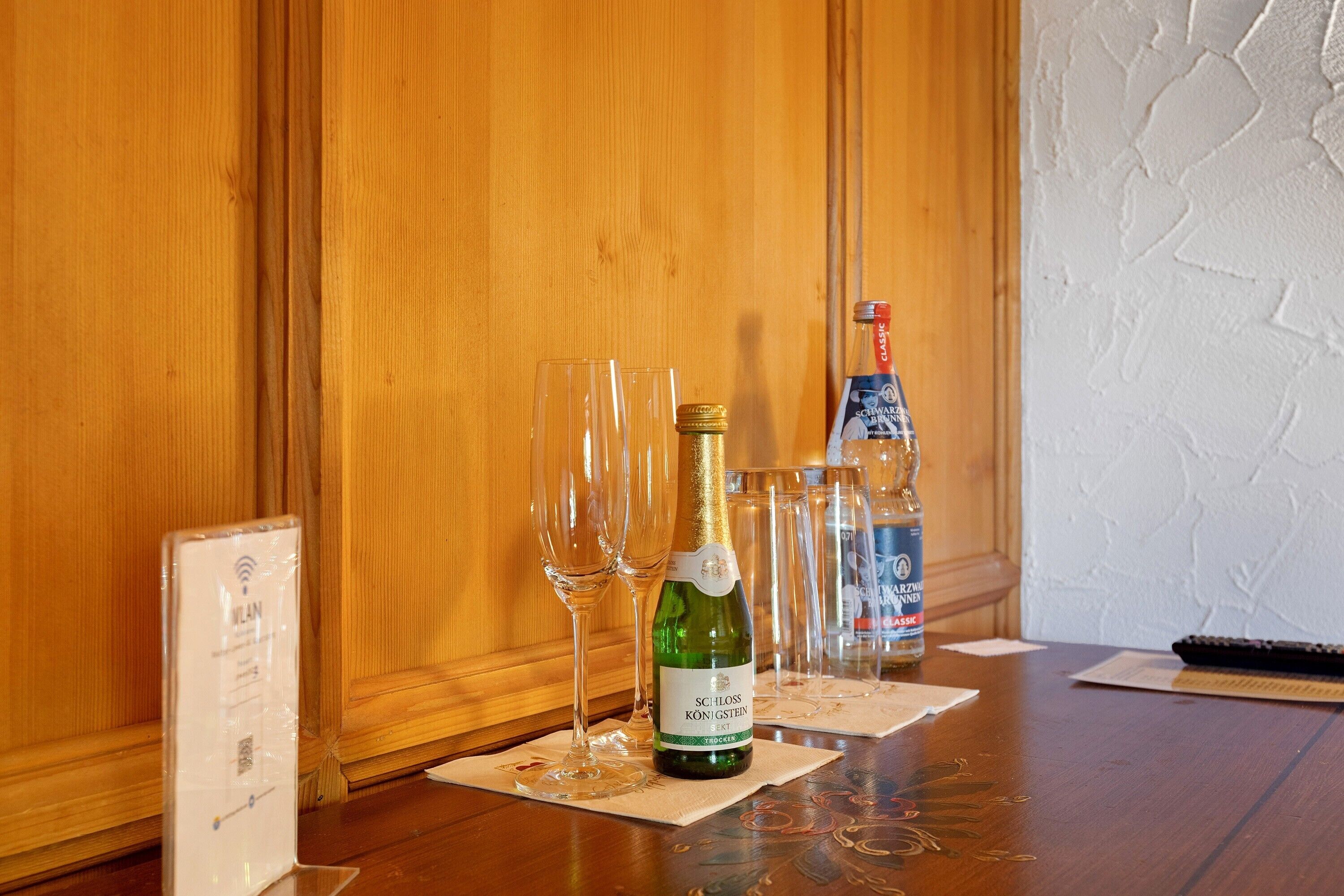 Una mesa de madera con una botella de vino SCILLOSS KON GÖSTEIN, varios vasos de vino vacíos y una botella de agua.