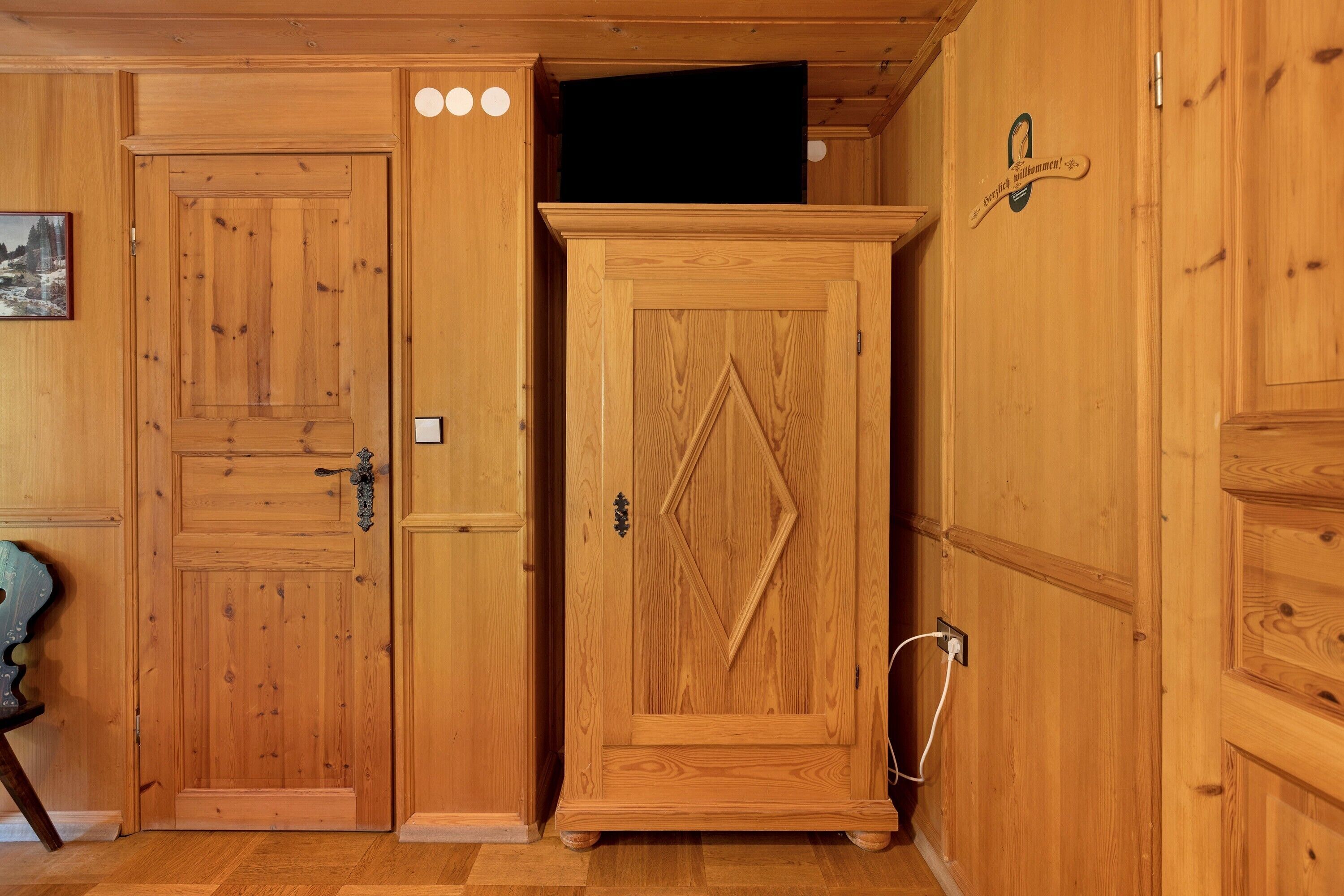 Una habitación de madera con una puerta cerrada, un armario y un televisor fijado a la pared.