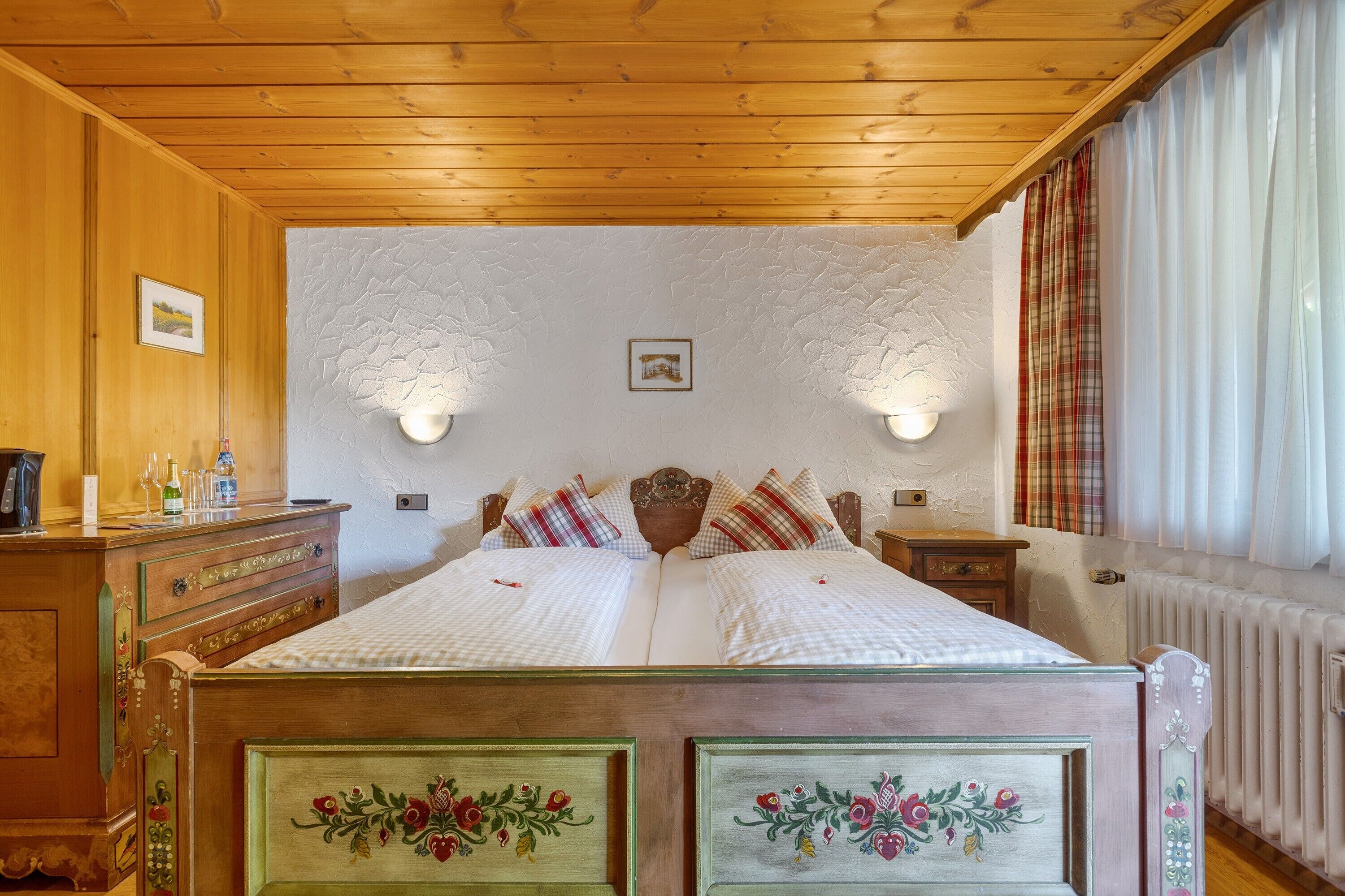 Una habitación con paneles de madera, una cama, dos lámparas de pared, un aparador y un radiador.