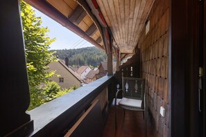 Un pasillo estrecho con techo de madera, una silla de metal y vistas a edificios y árboles.