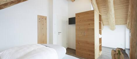 Een slaapkamer met een bed, een houten kledingkast en een televisie aan de muur.